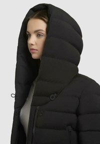 Giubbotto puffo nero con un grande cappuccio imbottito. Presenta una chiusura con zip e bottoni, una superficie liscia e un evidente motivo trapuntato orizzontale.