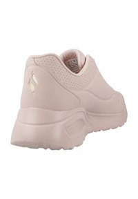 Zapatilla de deporte de color rosa claro con una textura suave, forma redondeada, acentos perforados y un collar acolchado. Presenta un logo sutil en el lado.