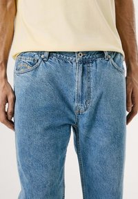 Jeans de mezclilla azul claro con un corte relajado, que cuentan con cierre de botón, bolsillos frontales y detalles de costura visibles.
