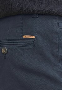 Dunkelblaue Hosen aus strukturiertem Stoff, mit einer vorderen Tasche, einem Knopf und einem Lederschild mit "JACK & JONES"-Markierung.