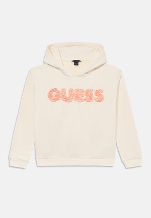 Sweat-shirt à capuche couleur crème avec des manches longues et un logo "GUESS" texturé en rose sur la poitrine.