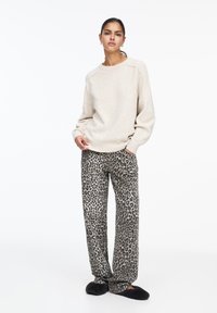 Pull beige à col rond, associé à un pantalon gris à imprimé léopard ample, et des pantoufles noires douces. Textures lisses dans l'ensemble.