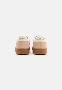 Rózsaszín velúr sportcipők fehér bőr kiegészítőkkel, barna gumitalppal és arany "Reebok" logóval a sarkán.