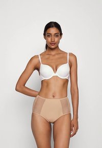 Balts krūšturis ar gludām kausiem un regulējamiem siksniņām, apvienots ar augsto vidukli gaiši nude krāsas apakšbiksēm, kurām ir sietiņveida sānu paneļi un bezšuvju dizains.