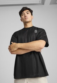Sort t-shirt med korte ærmer, der har strukturerede lodrette striber og et lille mærke med logo på venstre skulder. Materialet er en bomuldsblanding.