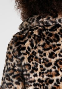 Faux pälsjacka med ett leopardmönster, med en mjuk, texturerad yta i nyanser av brunt och svart, som visar en klassisk kragsdesign.