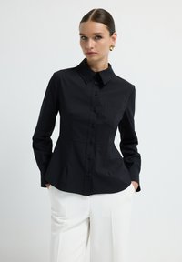 Camicia nera con bottone, realizzata in tessuto liscio, caratterizzata da un colletto classico, una tasca sul petto e una vestibilità slim con maniche lunghe.