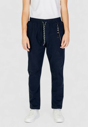 Pantaloni jogger blu navy con vita elastica, cordoncino regolabile, tasche laterali e dettaglio decorativo a catena. Texture liscia.