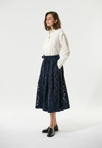 Hvid button-up skjorte parret med en navy blonde midi nederdel med blomster mønstre og en bundet talje. Båret med sorte loafers.