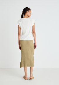 Bílý top s krátkým rukávem v kombinaci s ribbed midi sukní khaki barvy, s rozšířeným lemem a délkou až k kotníkům, doplněný sandály na pásky.