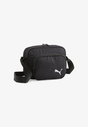 Czarna torba na ramię z regulowanym paskiem, przednią kieszenią na suwak oraz białym logo Puma w dolnym prawym rogu.