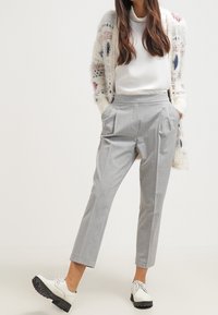 Šedé plisované kalhoty vyrobené z lehké tkaniny, s tapered střihem a bočními kapsami, doplněné bílým topem a černými lodičkami.