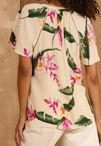 Kurzärmlige Bluse aus leichtem Stoff mit einem cremefarbenen Hintergrund, großen rosa und grünen Blumenmustern sowie Spitzenakzenten.
