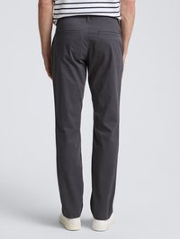 Homme portant un pantalon droit gris foncé, des baskets blanches et une chemise rayée, vu de dos sur un fond neutre.