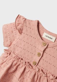 Robe en coton rose pâle avec de courtes manches volantées, motif œillet, fermeture à boutons et taille froncée. L'étiquette indique "Lil'Atelier."