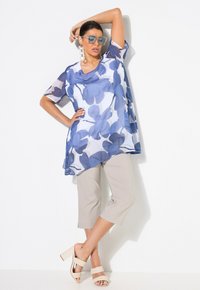 Leichtes, durchsichtiges Blusenshirt im blau-weißen Blumenmuster, kombiniert mit beigefarbenen, cropped Hosen und beigefarbenen, schlichten Sandaletten mit Absatz.
