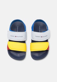 Kindersandaaltjes in marineblauw met witte, gele en rode bandjes, voorzien van het Tommy Hilfiger-logo op de witte klittenbandbandjes.