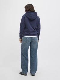 Felpa navy con cappuccio regolabile, abbinata a jeans blu a vita alta e gamba larga. Tessuto morbido con dettagli di cucitura minimi.