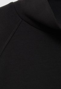 Gros plan sur un tissu noir montrant un col plié et un détail de couture sur un vêtement.