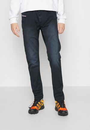 Pantalons en denim noir avec une légère texture, dotés de poches avant et d'une coupe ajustée, associés à des chaussures de sport de couleur vive.