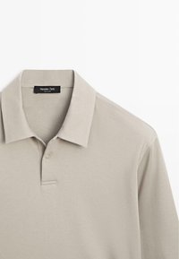 Beige poloshirt gemaakt van zacht materiaal met een klassieke kraag, drieknopenbies en subtiele stiknaden.