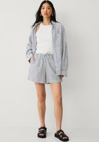 Chemise en coton rayée, débardeur blanc et short assorti. Les rayures sont bleues et blanches. Portez avec des sandales noires, dotées de bretelles épaisses et de semelles épaisses.
