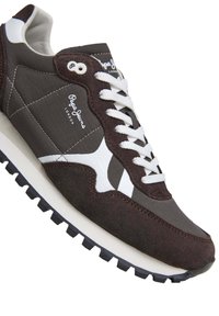 Zapatilla marrón y gris con acentos blancos, material de gamuza y tela, punta redondeada, cordones blancos, logo en el costado, suela negra texturizada.