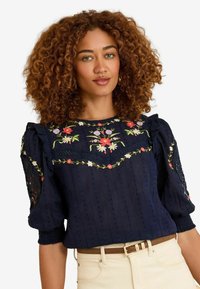 Navy blouse with floral embroidery on the chest and shoulders; textured fabric with puffed sleeves and lace accents on the sides.