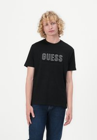 Svart bomulls T-skjorte med hvit "GUESS" logo over brystet, kort ermer, rund hals og avslappet passform.