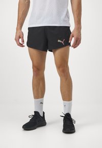 Czarne spodenki sportowe z delikatnym różowym logo PUMA. W zestawieniu z czarnymi sneakersami i białymi skarpetkami typu crew z brandingiem PUMA.