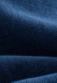 Denim w ciemnoniebieskim kolorze z diagonalną teksturą prążków, z lekkim połyskiem i miękkim, tkanym wykończeniem nałożonym na warstwowe fałdy.