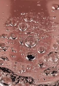 Heldere vloeistof met talloze luchtbellen en een roze achtergrond. De luchtbellen variëren in grootte, wat een gestructureerd oppervlakkeffect creëert.