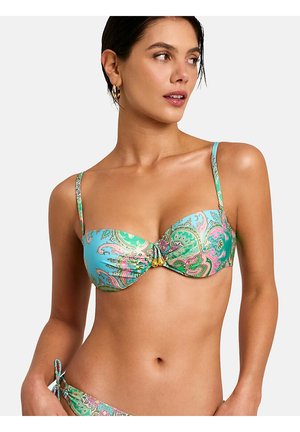 Femme portant un haut de bikini bleu et vert à imprimé cachemire avec des bretelles fines et des accents dorés, regardant vers sa gauche sur un fond neutre.