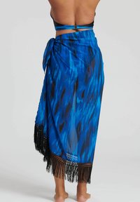 Blå genomskinlig omslagskjol med ett texturerat djurmönster och svart fransk trim längs nederkanten. Knyten i midjan med en knut.