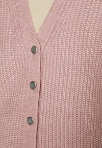 Rosa stickad kofta med V-ringning, med texturerat tyg, fem metallknappar fram och ribbad detalj längs kanterna.