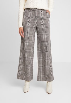 Woman wearing high-waisted, wide-leg checkered pants, cream cable-knit sweater, and white pointed-toe ankle boots, standing with hands in pockets.