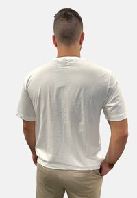 Weißes Baumwoll-T-Shirt mit kurzen Ärmeln und Rundhalsausschnitt, von hinten betrachtet. Der Stoff wirkt weich und leicht strukturiert.