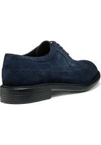 Zapato de vestir de ante azul marino con detalles de ala, cordones finos y suela de goma negra texturizada. Presenta perforaciones decorativas a lo largo de los bordes.