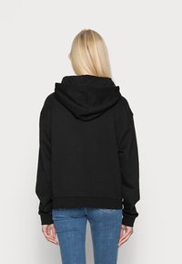 Felpa nera con cappuccio dal taglio rilassato, polsini elasticizzati e orlo che arriva sotto la vita, abbinata a jeans blu.