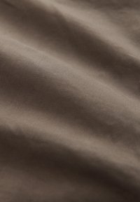 Zrnat rjav tkanina z gladko površino, ki prikazuje subtilne odtenke in gube, kar nakazuje mehkobo in prožnost.