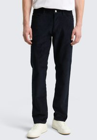 Granatowe spodnie sztruksowe o prostym kroju, z pięcioma kieszeniami i zapięciem na guzik z przodu, w połączeniu z białymi trampkami.