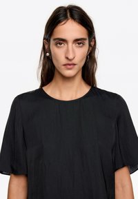 Czarna koszula z okrągłym dekoltem i krótkimi, luźnymi rękawami. Miękka tkanina o gładkiej fakturze. Prosty, nietożsiągnięty design.