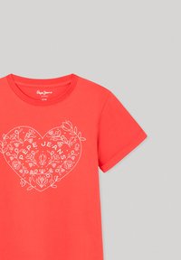 Camiseta corta roja de manga corta hecha de algodón, con un diseño de corazón blanco con elementos florales y texto "Pepe Jeans" en el centro.