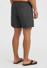 Shorts de bain noirs avec une taille élastique, une poche arrière et un tissu lisse et léger. Portés avec des tongs noires.