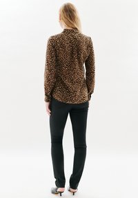 Camicia con stampa leopardata in marrone e nero, maniche lunghe, colletto e chiusura con bottoni sul retro. Abbinata a jeans skinny neri e tacchi.