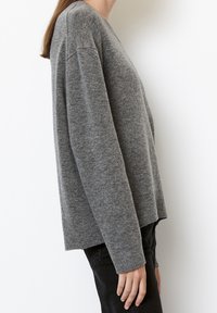 Maglione grigio a maglia con maniche lunghe, vestibilità rilassata e scollatura arrotondata. Il tessuto appare morbido con una finitura leggermente strutturata.
