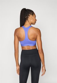 Μοβ αθλητικό σουτιέν με σχέδιο racerback, σε συνδυασμό με μαύρο κολάν ψηλής μέσης. Ομαλό ύφασμα με μινιμαλιστικό στυλ και χωρίς ορατά εξαρτήματα.