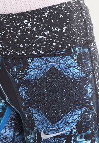 Leggings deportivos negros con patrones y texturas geométricas azules. Cuentan con una cintura alta y un pequeño logo blanco de Nike.