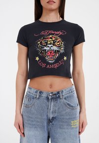 Sort krops T-shirt med et farverigt tiger grafik og teksten "Los Angeles". Parret med lyseblå højtaljede denimjeans.