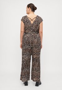 Jumpsuit z leopardjim vzorcem, kratkimi rokavi, z ožjim pasom in krščanskim detajlom na hrbtu. Tokratna tkanina in širok kroj hlač. Črna obutev.
